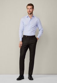 Lichtblauwe, lange mouwen overhemd met knopen, gecombineerd met donkerbruine op maat gemaakte broeken. De broek heeft een enkele knoop en elegante zwarte schoenen.