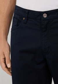 Chinos azul marino de tela de mezcla de algodón. Presenta un bolsillo frontal, cierre de botón y detalles de costura visibles. Textura suave.