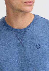 Blue cotton sweatshirt featuring a ribbed crew neck and decorative stitching. A small navy logo is visible on the chest area.