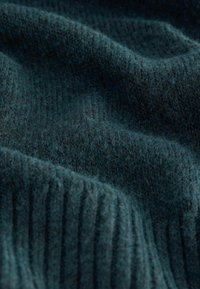 Tmavomodrý textil s jemným, štruktúrovaným povrchom, ktorý má jemné rebrovanie a mierne variácie v hĺbke farby, naznačujúce pletený dizajn.