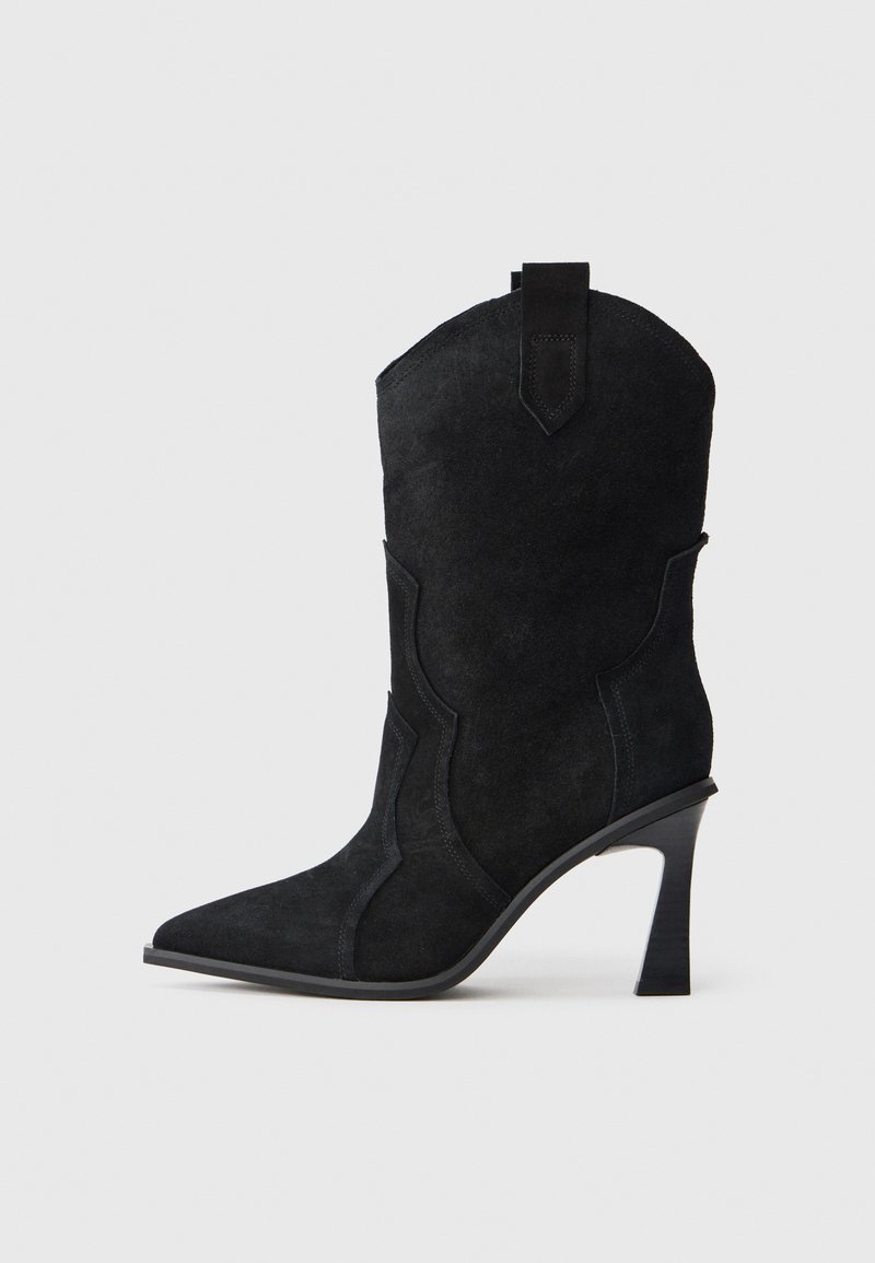 Stivale da cowboy in suede nero con punta a punta, alto tacco a stiletto e cuciture decorative lungo il gambo. Presenta una linguetta sulla parte superiore.