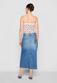 Hvit crop top med rød og svart tekstmønster; blå denimskjørt med stjernemønster og rå kant; blå hæl sandaler; bakfra.