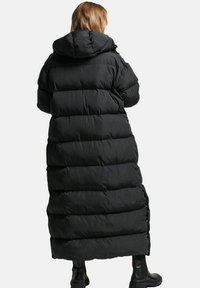 Sort pufferjakke, lang længde med hætte, quiltet design og sidelommer. Glat tekstur med indsnævret talje og justerbare snore.