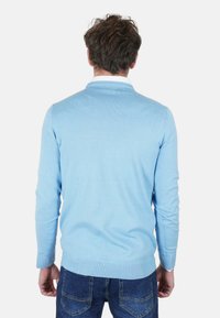 Maglione azzurro chiaro in maglia con scollo e polsini a coste, caratterizzato da una texture liscia e una forma aderente, abbinato a jeans blu scuro.