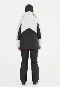 Skijacke und -hose Set in Weiß und Schwarz, mit modernem Design, hoher Kragen und verstellbaren Bündchen. Der Stoff sieht strukturiert aus.