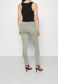 Jeans ajustados de suave tela verde claro con una textura lisa. Cuentan con una cintura de altura media y dos bolsillos en la parte posterior. Combinados con una parte superior negra.