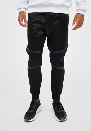 Pantalones deportivos negros hechos de tela suave, con detalles texturizados en los costados, puños ajustados y franjas horizontales a lo largo de los muslos.