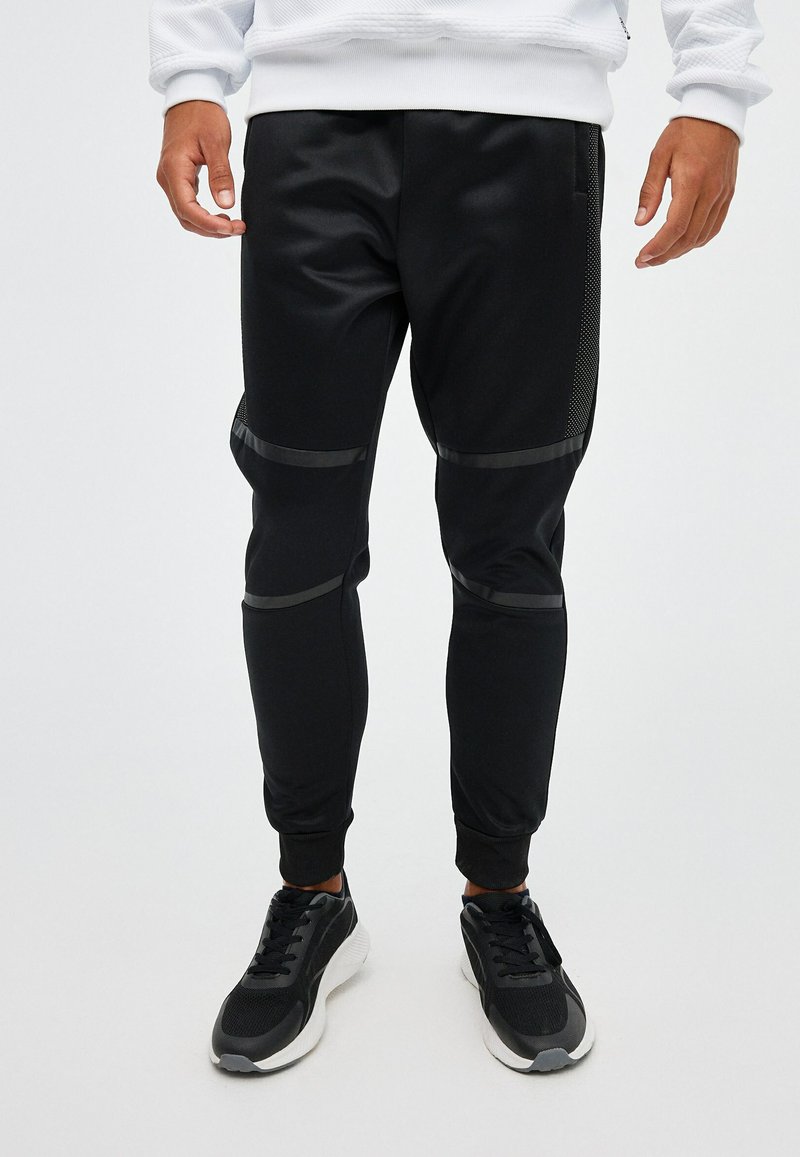 Pantalones deportivos negros hechos de tela suave, con detalles texturizados en los costados, puños ajustados y franjas horizontales a lo largo de los muslos.