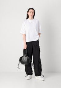 Hvit kortermet oversized t-skjorte med en liten logo, kombinert med svarte cargo-bukser og en svart handbag. Hvite joggesko fullfører antrekket.