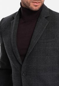 Szary marynarka w jodełkę o dopasowanym kroju, z klapą z wycięciem i pojedynczym guzikiem, noszona na ciemnym golfie.