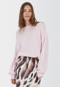 Helles pinkes Strickpullover mit lockerer Passform, gerippten Bündchen und rundem Ausschnitt, kombiniert mit einem gemusterten Rock in erdigen Tönen.