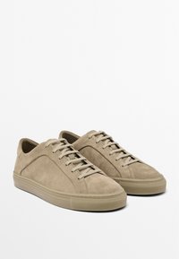 Beige suede sneakers with a low profile, rounded toe, and tonal laces. Features a textured upper and smooth rubber sole.