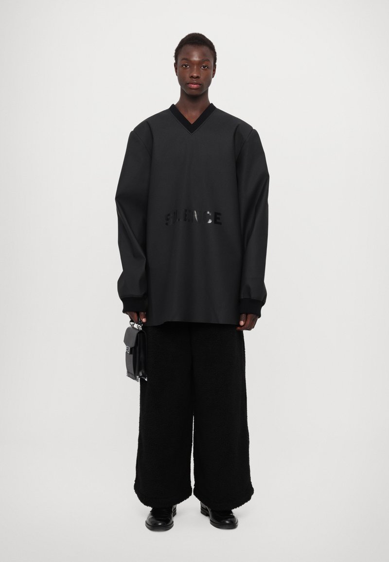 Sweatshirt noir surdimensionné avec un col en V, doté d'un texte découpé "SILENCE". Associé à un pantalon large noir texturé et des chaussures noires brillantes.