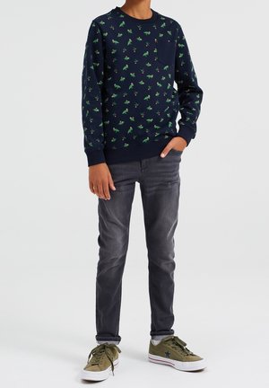 Sweat-shirt bleu marine avec imprimé dinosaure vert, col rond, manches longues et poche avant. Associé à un jean gris et des baskets olive.