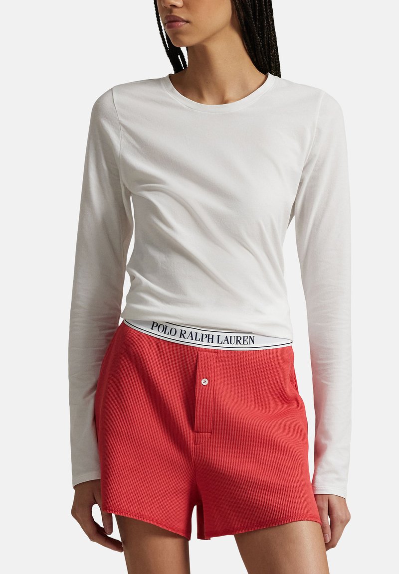 Vit långärmad topp i bomull kombinerad med röda ribbade shorts med logoband i midjan och knäppning framtill.