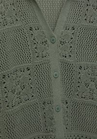 Ljusgrön stickad cardigan med v-öppning, knappstängning och dekorativa spetssmönster med en strukturerad, öppen vävdesign.