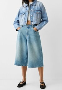 Hellblaue cropped Jeansjacke mit zwei vorderen Taschen, kombiniert mit weiten, locker sitzenden hellblauen Jeans-Culottes und schwarzen Mesh-Ballerinas.