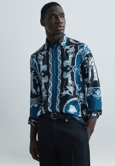 Camicia con motivo nero e blu con dettagli in argento, dotata di colletto, bottoni e maniche lunghe, abbinata a pantaloni neri.