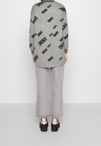 Pull gris surdimensionné avec logo DKNY noir imprimé, manches longues, poignets côtelés, assorti à un pantalon large gris clair et des chaussures noires épaisses.