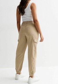 Khaki spodnie cargo z elastycznym pasem, zwężanymi mankietami, kieszeniami bocznymi i tylnymi. W zestawie z białymi trampkami i topem bez rękawów.