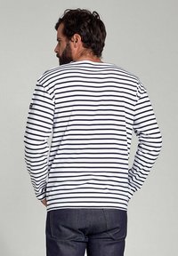 Langærmet stribet skjorte i marineblå og hvid bomuld. Har crew neck og afslappet pasform. Bortset fra de mørke jeans, vises bagfra.