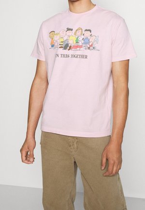 Hellrosa Baumwoll-T-Shirt mit den Cartoonfiguren aus "Peanuts" und dem Text "IN THIS TOGETHER" zentriert unter der Grafik.
