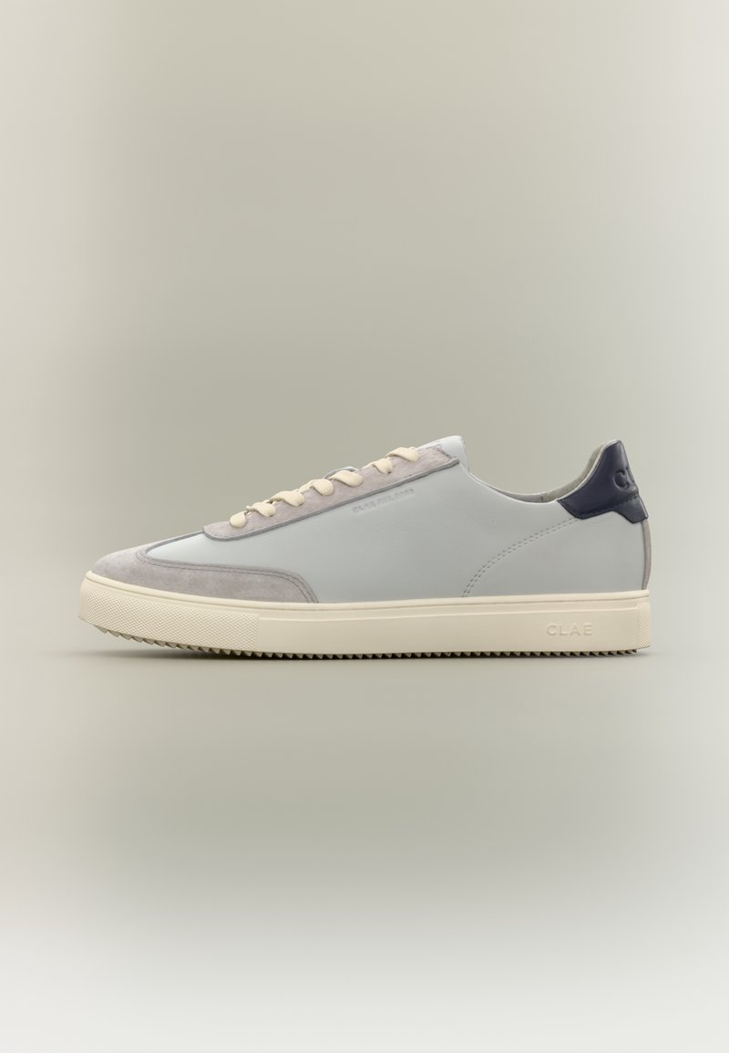 Basket basse gris clair avec semelle beige, lacets écru, embout en daim et languette de talon foncée, vue de profil sur un fond uni.
