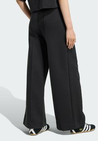 Pantalones de chándal negros de pierna ancha con una textura suave, que presentan costuras laterales y una cinturilla cómoda, combinados con zapatillas deportivas en blanco y negro.