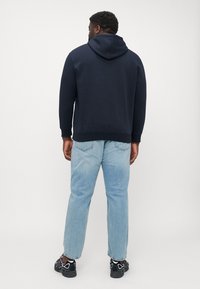 Marineblauwe hoodie met een kangoeroezak en een capuchon met trekkoord, gecombineerd met lichtblauwe jeans en zwarte sportschoenen, dat een comfortabele pasvorm toont.