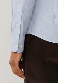 Lichtblauw geblokt shirt met een puntkraag, knoopmanchetten en beige knopen, gecombineerd met donkere corduroy broek.