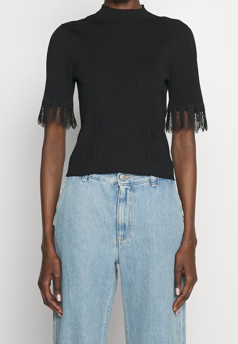 Haut noir côtelé à manches courtes avec bordure en dentelle sur les manches, porté avec un jean en denim bleu clair taille haute.