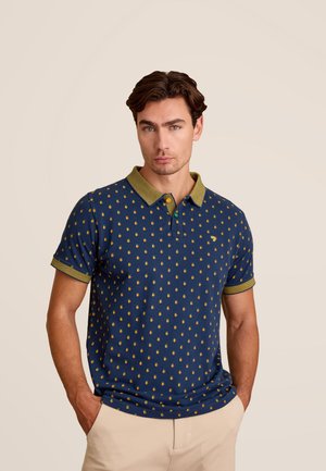 Marineblauwe poloshirt met geel ananaspatroon, groene ribgebreide kraag en manchetten. Stof is getextureerd, met korte mouwen en een getailleerde pasvorm.