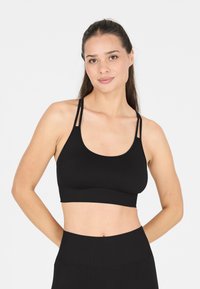 Soutien-gorge de sport noir avec un décolleté en forme de cuillère, des bretelles fines réglables et une texture extensible à rayures. Assorti à des leggings noirs taille haute.