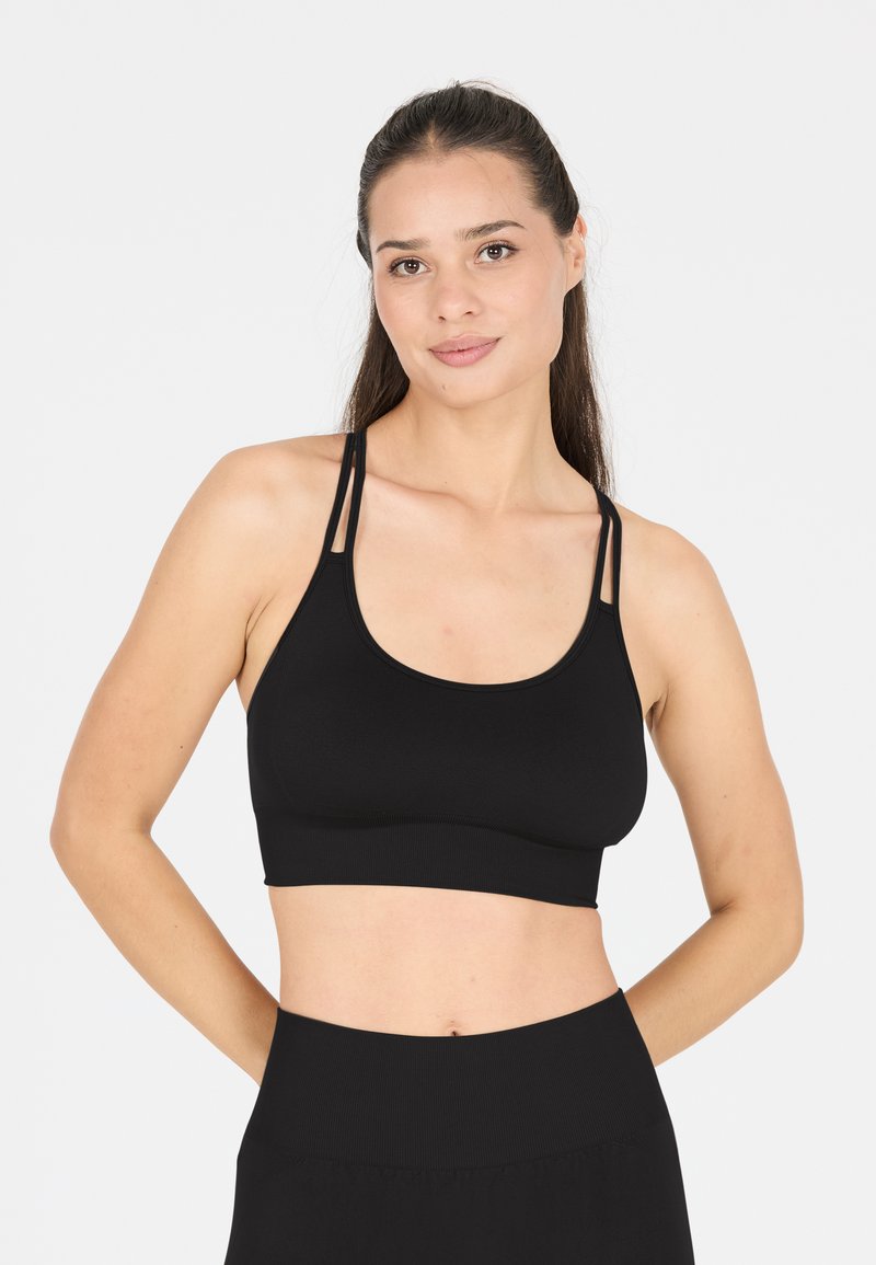 Soutien-gorge de sport noir avec un décolleté en forme de cuillère, des bretelles fines réglables et une texture extensible à rayures. Assorti à des leggings noirs taille haute.