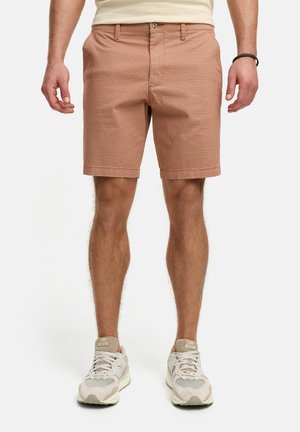 Licht roestkleurige shorts met een geometrisch patroon, een vlakke voorkant, zijzakken en omgeslagen zomen. Gecombineerd met beige sneakers.