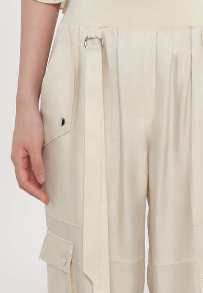 Beige Cargo-Hosen mit seidiger Textur, ausgestattet mit Seitentaschen, einem Gürtelschlaufen und einem flachen Bund. Silberne Druckknopfdetails setzen Akzente im Design.