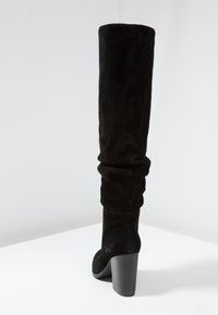 Bottes noires en suède montant jusqu'au genou avec un design ample et un talon épais. La chaussure présente une texture lisse et un bout effilé.