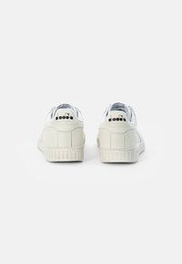 Baskets blanches en cuir avec des accents texturés, semelle en caoutchouc nervurée et doublure intérieure bleue. Présente le logo de la marque sur le talon et la languette.