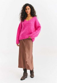 Ružový plyšový sveter s véčkovým výstrihom a nadrozmernými rukávmi, skombinovaný s hnedou saténovou maxi sukňou a hnedými členkovými čižmami s prackami.