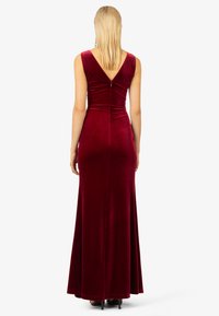 Langes, tailliertes burgunderfarbenes Samtkleid mit V-förmigem Rückendesign und bodenlangem Saum. Sanfte Textur und minimalistische Nähte, ausgestattet mit einem dezenten Reißverschluss.