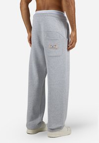 Mand iført løstsiddende grå træningsbukser med en baglomme, der har et mærke, der står "Pegador Everyday Ambition", og hvide sneakers, vist bagfra.
