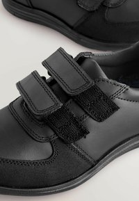 Scarpe nere in materiale sintetico con tre cinturini in velcro, tomaia texturizzata e suola piatta in gomma.