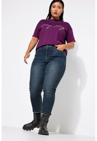 Camiseta violeta con texto en blanco, combinada con jeans skinny de color azul oscuro y botas de tobillo negras con un patrón de hilo.
