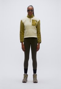 Φλις πουλόβερ σε ανοιχτό μπεζ και ελιά, με φερμουάρ στο λαιμό, μπροστινή τσέπη, συνδυασμένο με κολάν σε ελιά και γκρίζα ορειβατικά μποτάκια.