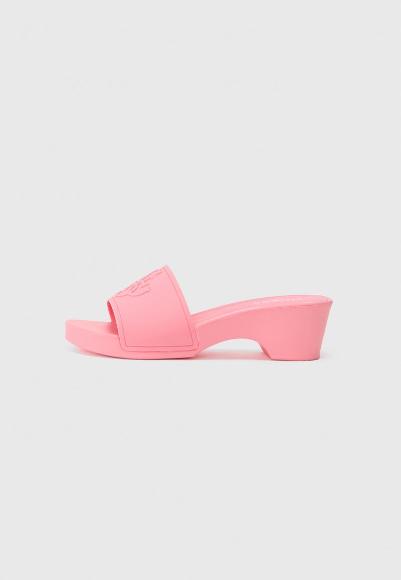 Rosa glidesandal med brede stropper og en liten hæl. Laget av glatt gummiliknende materiale, med pregede detaljer på stroppen.