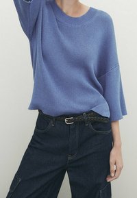 Pull tricot bleu clair avec un col large et des manches trois-quarts, assorti à un jean en denim foncé et une ceinture noire tressée.