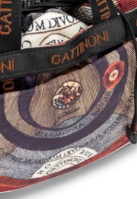 Grande borsa in tessuto con intricati modelli circolari in rosso, viola e beige, con una tracolla nera a contrasto stampata con "GATINONI."