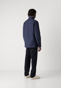 Námořnická prošívaná bunda s vysokým límcem, rovný střih a patentky na boku, kombinovaná s tmavými kalhotami a světlými teniskami.