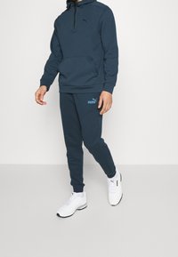 Felpa blu navy con collo a mezzo zip, tasca a marsupio e logo. Pantaloni da sudore affusolati abbinati dello stesso colore, abbinati a sneaker bianche.