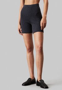 Shorts oscuros de mezcla de algodón con un diseño acanalado y cintura alta, que presentan una pequeña etiqueta con el logo en la cinturilla y una silueta ajustada.